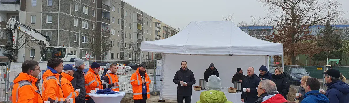 Menschengruppe die in einem Kreis vor einem weißen Zelt steht. 