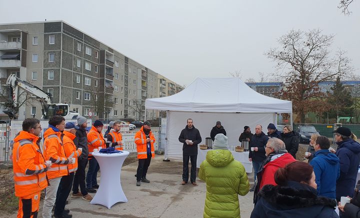 Menschengruppe die in einem Kreis vor einem weißen Zelt steht. 