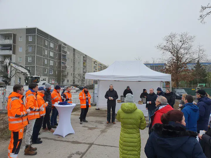 Menschengruppe die in einem Kreis vor einem weißen Zelt steht. 