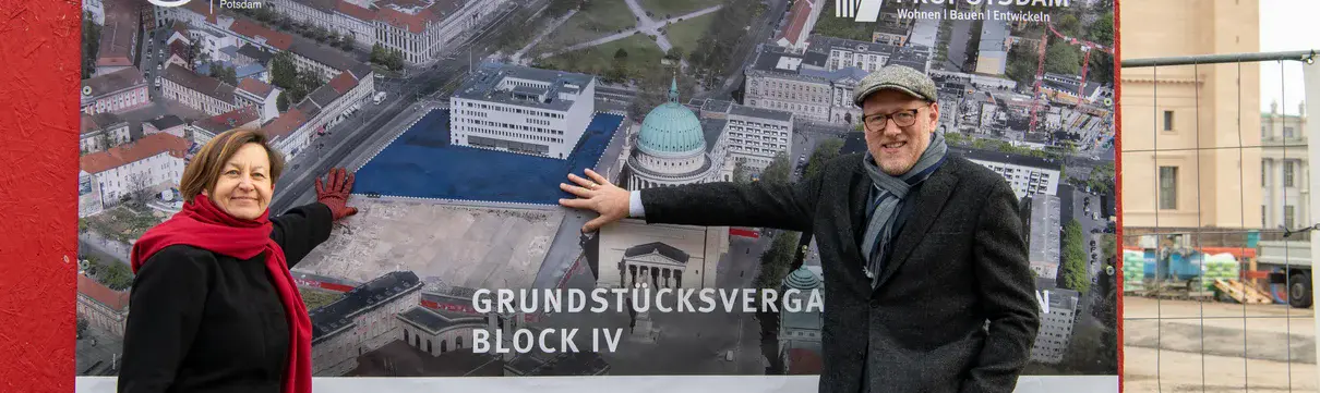 Die Geschäftsführerin und der Geschäftsführer des Sanierungsträgers Potsdam stehen in Winterkleidung vor einer Bildtafel mit den Entwürfen für neue Gebäude.