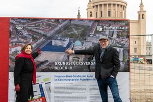 Die Geschäftsführerin und der Geschäftsführer des Sanierungsträgers Potsdam stehen in Winterkleidung vor einer Bildtafel mit den Entwürfen für neue Gebäude. 