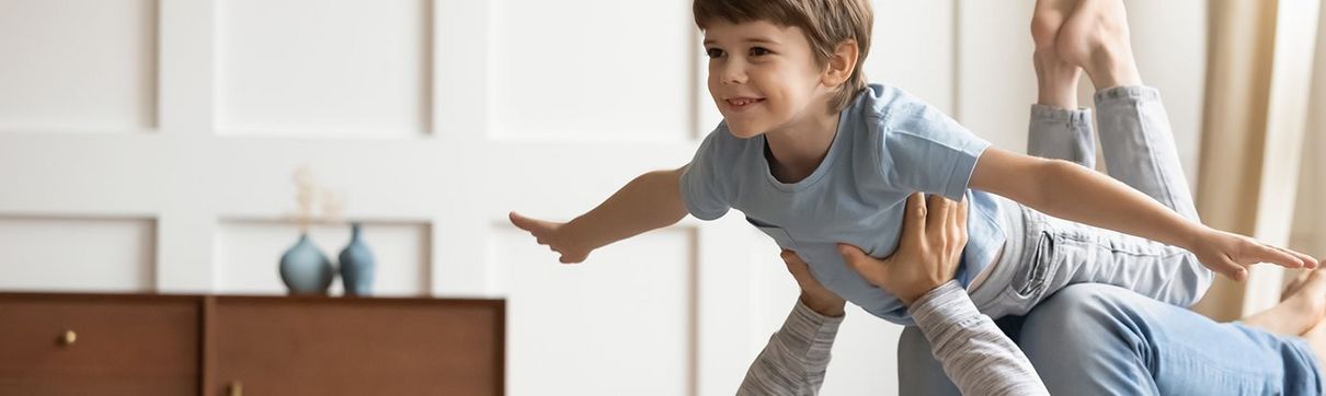 Vater liegt zu Hause auf dem Teppichboden und hält Sohn wie ein Flugzeug in der Luft.