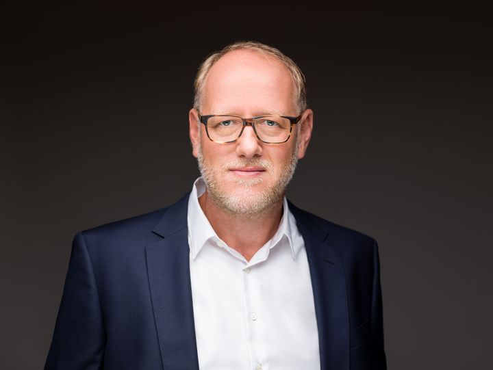 Geschäftsführer der ProPotsdam GmbH, Bert Nicke, in weißem Hemd und blauem Jacket schaut freundlich vor dunklem Hintergrund