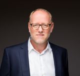 Geschäftsführer der ProPotsdam GmbH, Bert Nicke, in weißem Hemd und blauem Jacket schaut freundlich vor dunklem Hintergrund