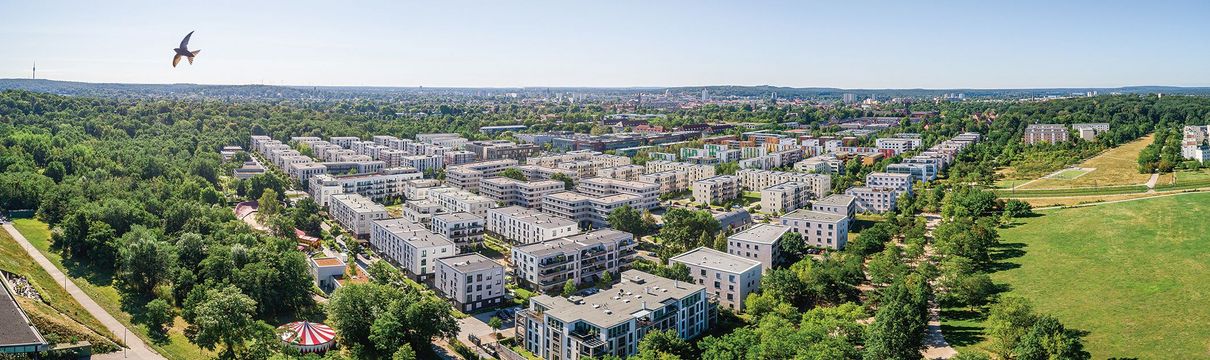 Luftaufnahme über viergeschossige Wohnhaussiedlung umgeben von Baumbestand und Park