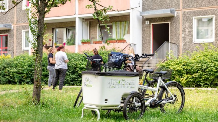 Grüner Wohnhof mit Lastenrad im Vordergrund, im Hintergrund unterhalten sich Menschen