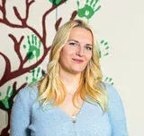 Eine Frau steht vor einer Wand, auf der ein Baum und eine blau-weiße Lilie gemalt sind.