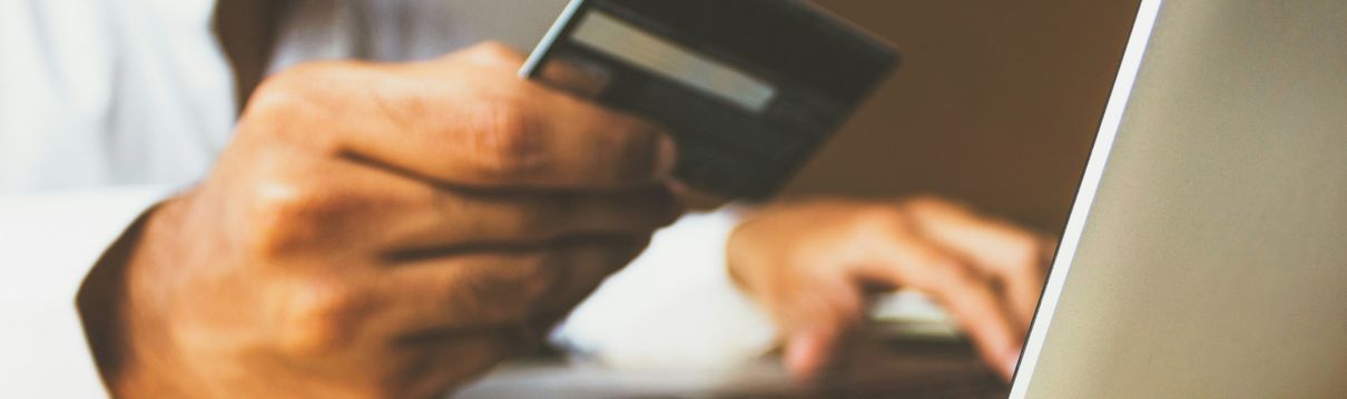 Nahaufnahme eines Laptop und einer Hand, die eine Bankkarte hält