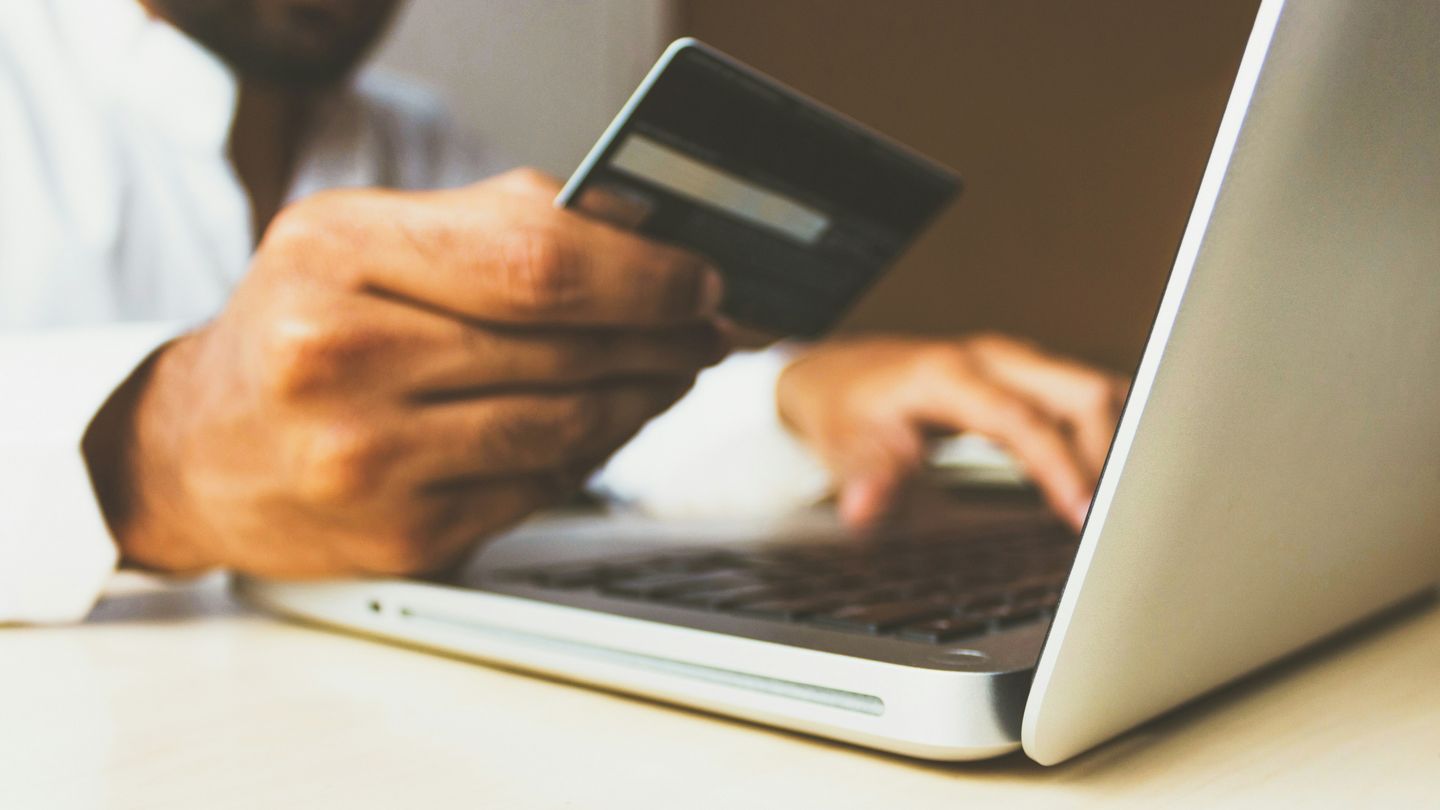 Nahaufnahme eines Laptop und einer Hand, die eine Bankkarte hält