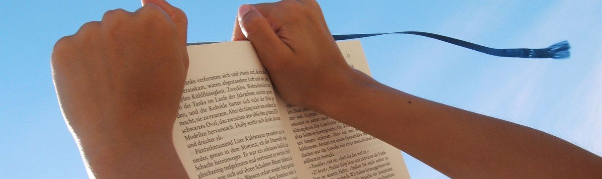 Zwei Hände halten ein offenes Buch in den Himmel