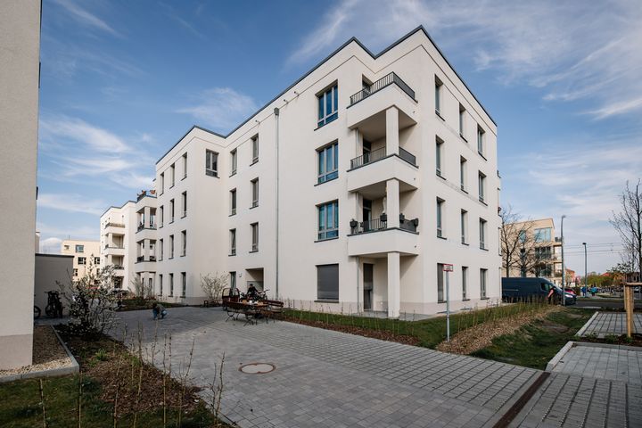 Modernes, helles Mehrfamilienhaus mit vier Stockwerken und Balkonen in einem neu angelegten Wohnquartier mit Gehwegen und blauem Himmel