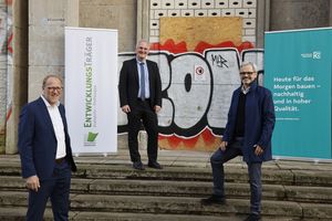 Drei Männer im Anzug, der Geschäftsführer des Entwicklungsträgers Potsdam, der Baubeigeordnete der Stadt und der Chefentwickler der Deutsche Wohnen, stehen vor einem alten, mit Graffiti besprühten Gebäude. Im Hintergrund sind Werbebanner zu sehen.