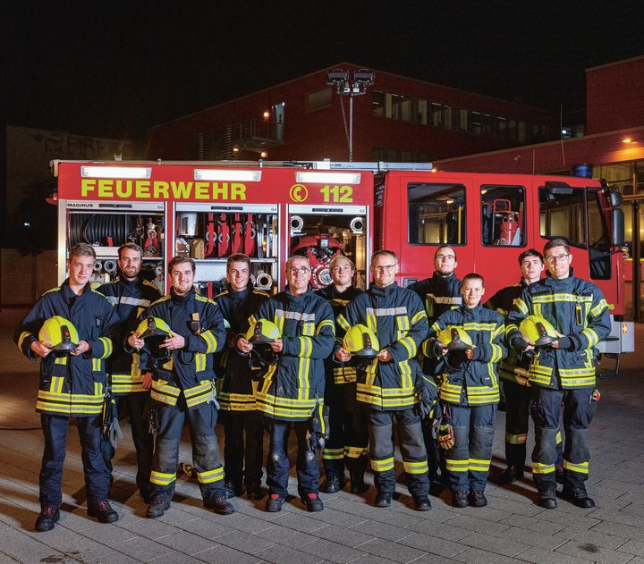 Eine mehrköpfige Feuerwehrmannschaft steht in der Dunkelheit vor einem Feuerwehrfahrzeug