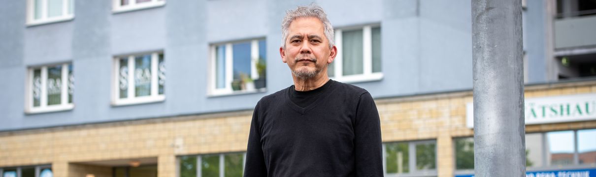 Ein Mann mit Bart steht vor einem Hochhaus.