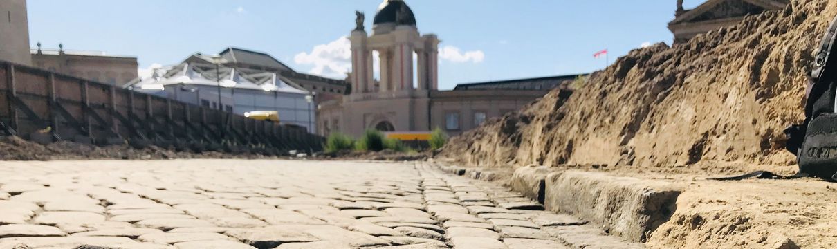 Alter Markt_Historisches Straßenpflaster Straßenplaster, das am unteren Bildrand aufgebrochen ist. Rechts zieht sich ein Sandhügel entlang.