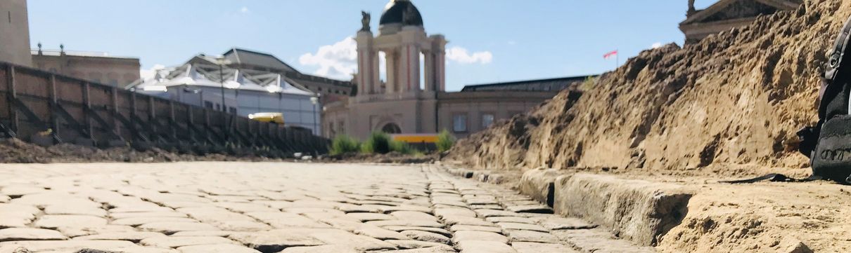 Alter Markt_Historisches Straßenpflaster Straßenplaster, das am unteren Bildrand aufgebrochen ist. Rechts zieht sich ein Sandhügel entlang.
