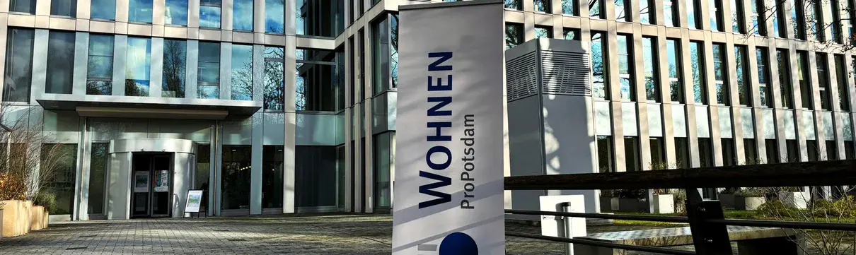 Vor einem großen Gebäude mit vielen Fenstern steht ein Banner mit der Aufschrift ProPotsdam Wohnen.