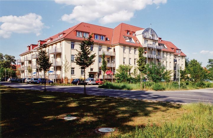 Ein saniertes Kasernen-Gebäude mit einer Straße davor und grünen Wiesen ringsherum.