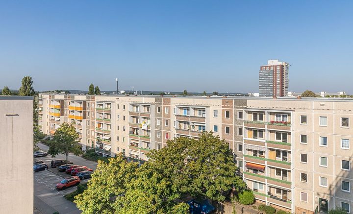Straßenqueransicht mit grauen Plattenbauten und blauem Himmel. 