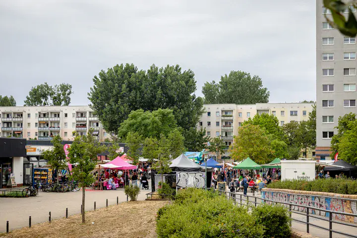 Stadtteilfest auf einem Platz zwischen Wohngebäuden mit Pavillons, Besuchergruppen und Marktständen.