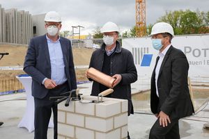 Der ProPotsdam-Geschäftsführer, ein Architekt und der Oberbürgermeister stehen auf einer Baustelle. Alle tragen wei0e Schutzhelme. Der Architekt hält eine Zeitkapsel in der Hand. Im Hintergrund sind ein Banner der ProPotsdam und ein Kran zu sehen. 