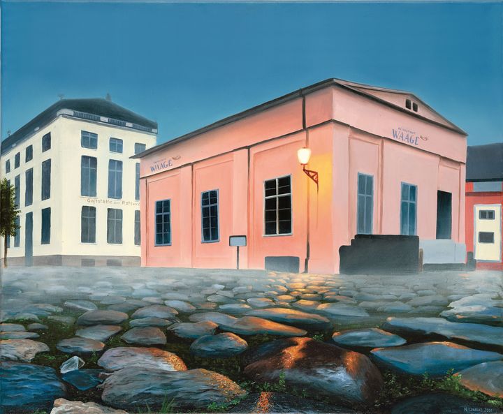 Ein kleines rosafarbenes Haus in der Bildmitte, an deren Hauswand eine Außenleuchte ihr gelbes Licht auf die Gehwegsteine im Bildervordergrund wirft