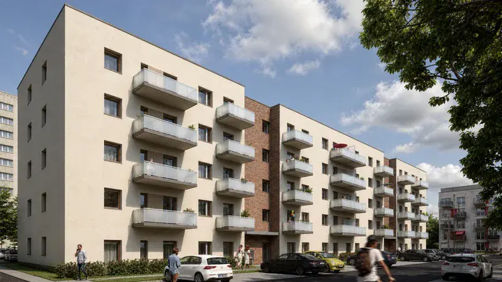 Moderne, mehrstöckige Wohngebäude in heller Putz- und Klinkerbauweise mit zahlreichen Balkonen, davor parkende Autos und Passanten unter blauem Himmel.