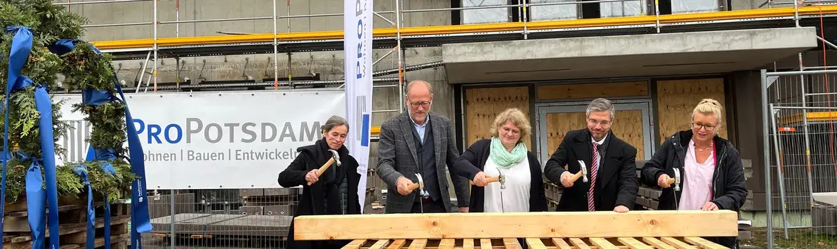 Geschäftsführer der ProPotsdam, der Oberbürgermeister und weitere Akteure hämmern Nägel in einen Holzbalken ein.