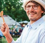 Matthias Michel blickt lächeln in die Kamera und hält einen Holzlöffel hoch