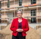 Die Bundesbauministerin steht auf einer Baustelle vor einem eingerüsteten Gebäude.