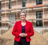 Die Bundesbauministerin steht auf einer Baustelle vor einem eingerüsteten Gebäude.