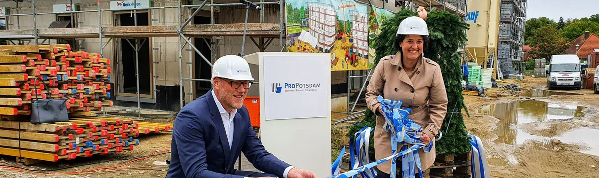Der Geschäftsführer der ProPotsdam und die Sozialbeigeordnete stehen mit weißen Helmen vor einem Haus, das noch fertiggebaut wird.