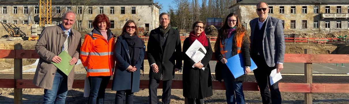 Sieben Menschen, darunter Oberbürgermeister Mike Schubert, Baubeigeordneter Bernd Rubelt und Entwicklungsträger-Potsdam-Geschäftsführer Bert Nicke, stehen vor einer Baustelle in Krampnitz.