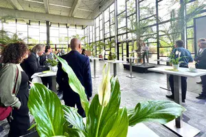 Mehrere Menschen stehen in der Biosphäre Potsdam an kleinen Tischen und hören ProPotsdam-Geschäftsführer Bert Nicke zu, der auf einer kleinen Bühne vor einem Mikrofon steht.  