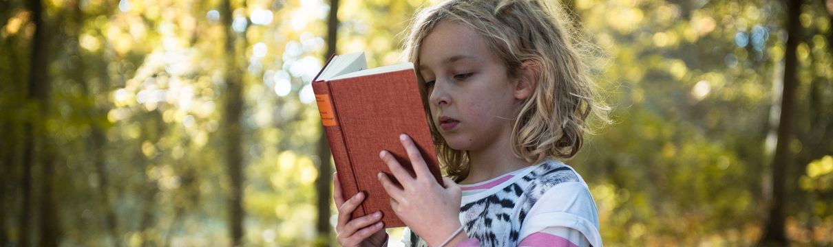 Ein kleines Mädchen liest in einem Buch im Volkspark.