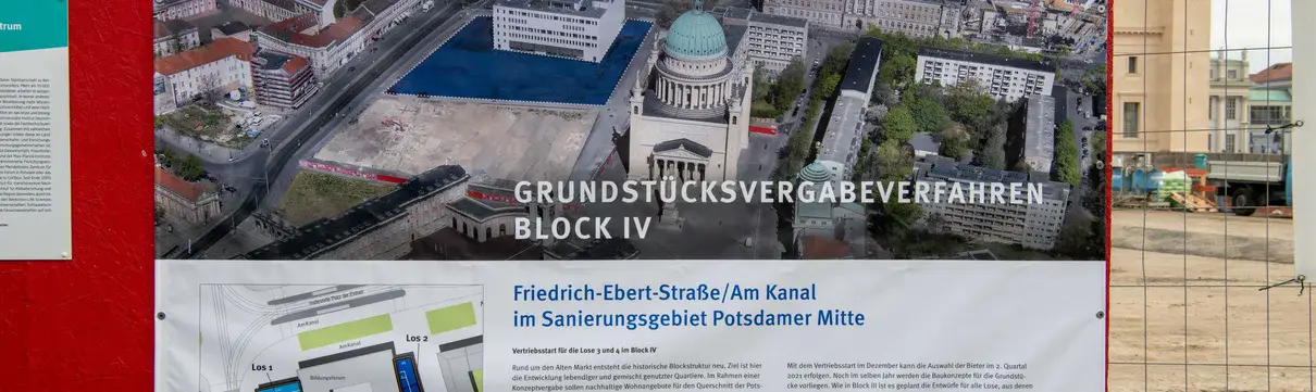 Ein Banner mit der Aufschrift "Grundstücksvergabeverfahren Block IV" und dem Logo der ProPotsdam hängt an einem Bauzaun. Im Hintergrund ist ein historisches Kirchengebäude zu sehen.
