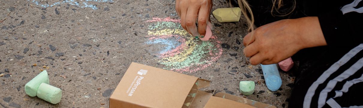 Kind malt mit Kreide einen Regenbogen auf den Asphalt