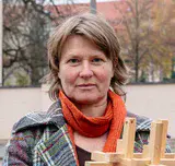 Kurzhaarige Frau mit orangem Schal steht mit einem Holzmodell in der Hand an einer Potsdamer Straßenecke