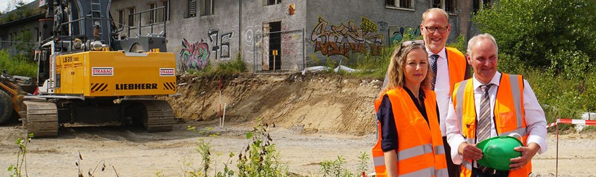 Der Geschäftsführer des Entwicklungsträgers Potsdam steht zusammen mit dem Baubeigeordneten und der Staatssekretärin für Finazen vor einem verfallen aussehenden Gebäude. Sie tragen orangene Warnwesten und halten Bauhelme in der Hand.