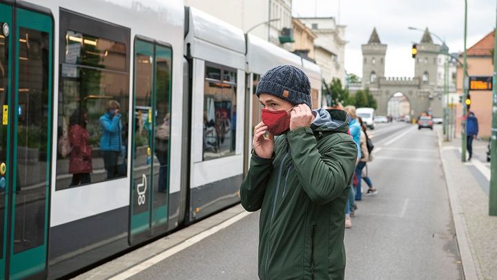 Mann mit Schutzmaske im Gesicht will in eingefahrene Straßenbahn einsteigen