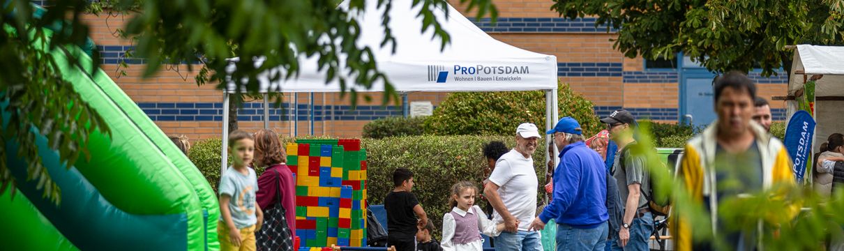 Nachbarschaftsfest im Freien mit Spielangeboten, Hüpfburg und Menschen zwischen Bäumen und Pavillons.
