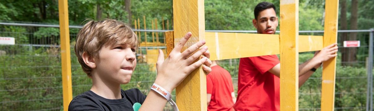 Ein Junge und ein junger Mann halten ein Holzgerüst fest.