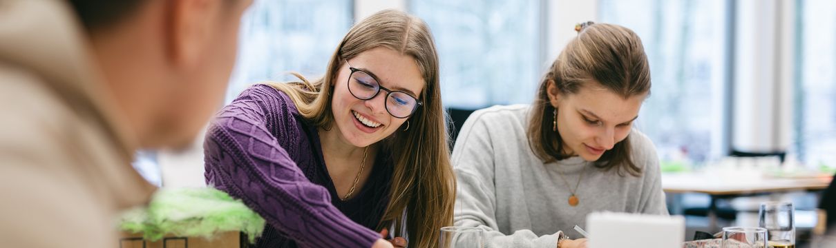 Auf dem Foto sind Schülerinnen und Schüler in einem Klassenraum an Tischen zu sehen, die an Modellen arbeiten. 