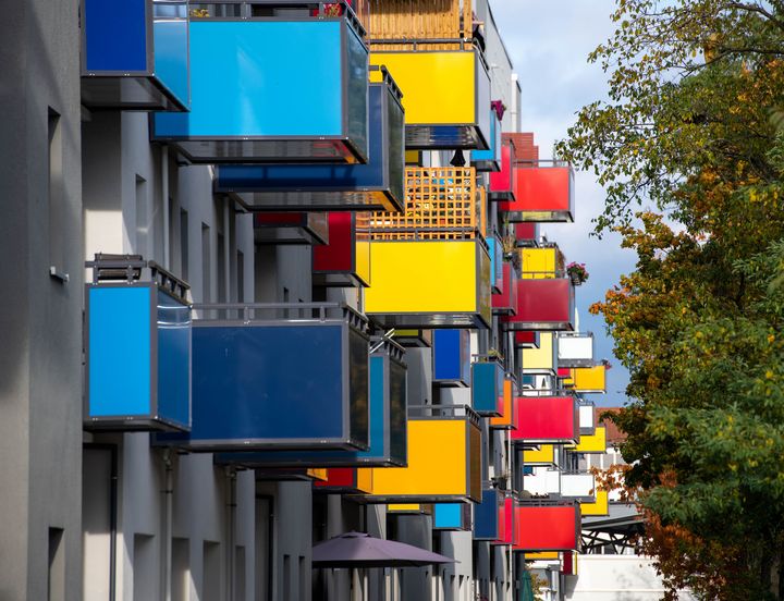 Blaue, gelbe, orange und weiße Balkone entlang der Häuserzeile in der Konrad-Wolf-Allee