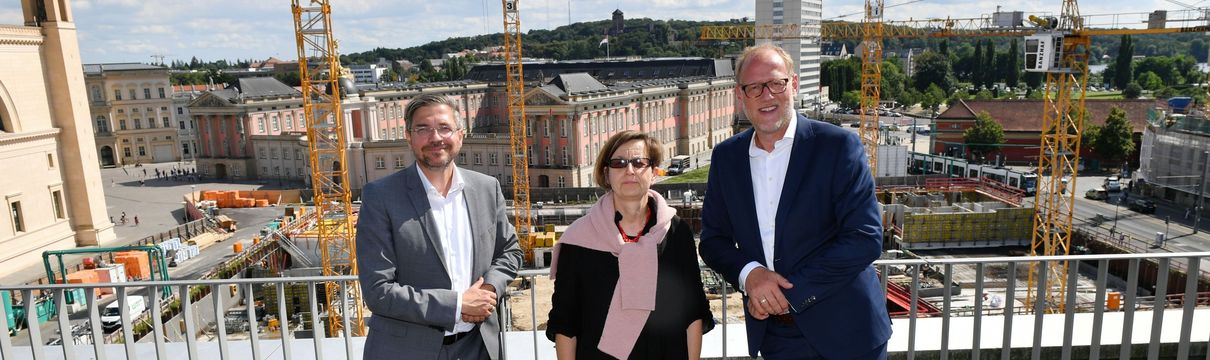 Die Geschäftsführer des Sanierungsträgers Potsdam und der Oberbürgermeister stehen an einer Baustelle. Im Hintergrund sind große Baukräne zu sehen.
