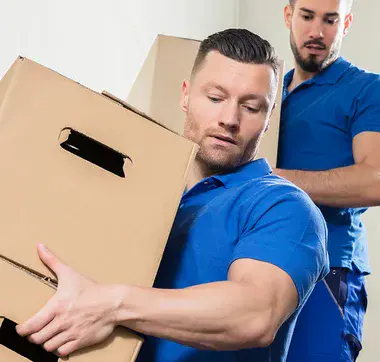 Treppenhaus, in dem zwei Männer in blauer Arbeitskleidung Umzugkartons von oben nach unten tragen