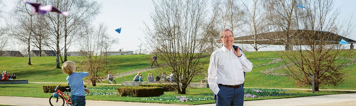 Matthias Platz, rechts, steht im Volkspark und lächelt, links neben ihm lässt ein kleiner Junge Papierflieger steigen.