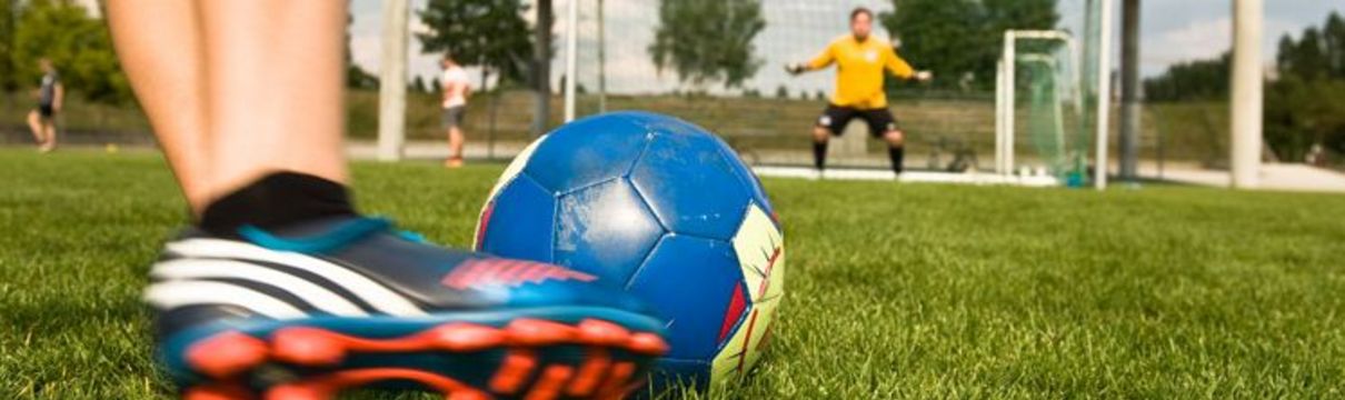 Ein Junge schießt mit einem Fußball auf ein Tor, in dem ein anderer Junge steht.