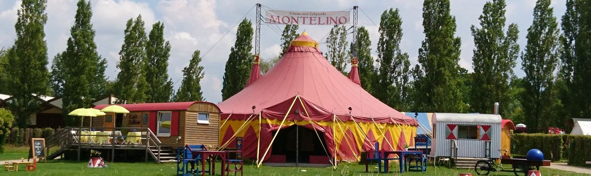 Ein rotes Zirkuszelt auf einer Wiese mit Bäumen im Hintergrund