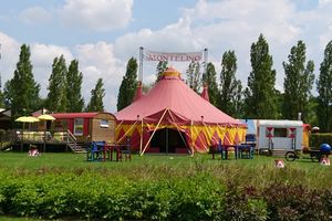Ein rotes Zirkuszelt auf einer Wiese mit Bäumen im Hintergrund